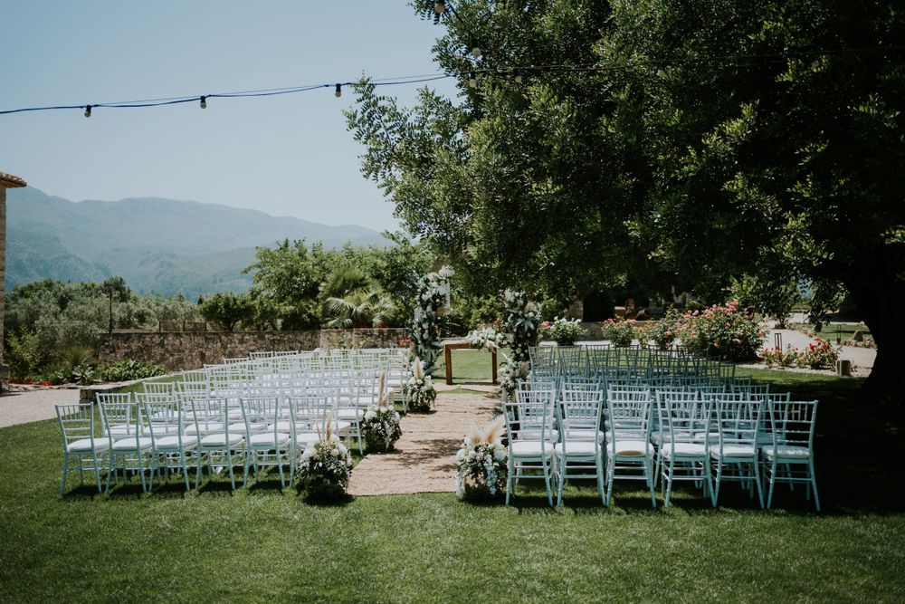 Outdoor wedding ceremony setup with white chairs and floral decorations in a garden overlooking mountains.