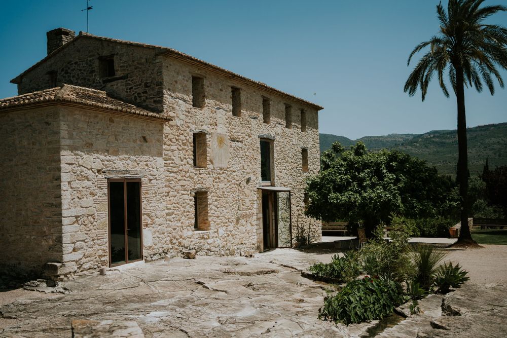Ancient stone villa with traditional Mediterranean architecture and palm tree in natural surroundings.