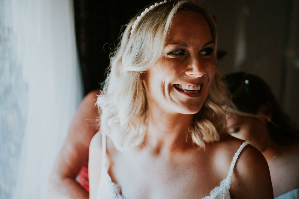 Candid bridal preparation moment showing joyful expression and detailed lace gown.
