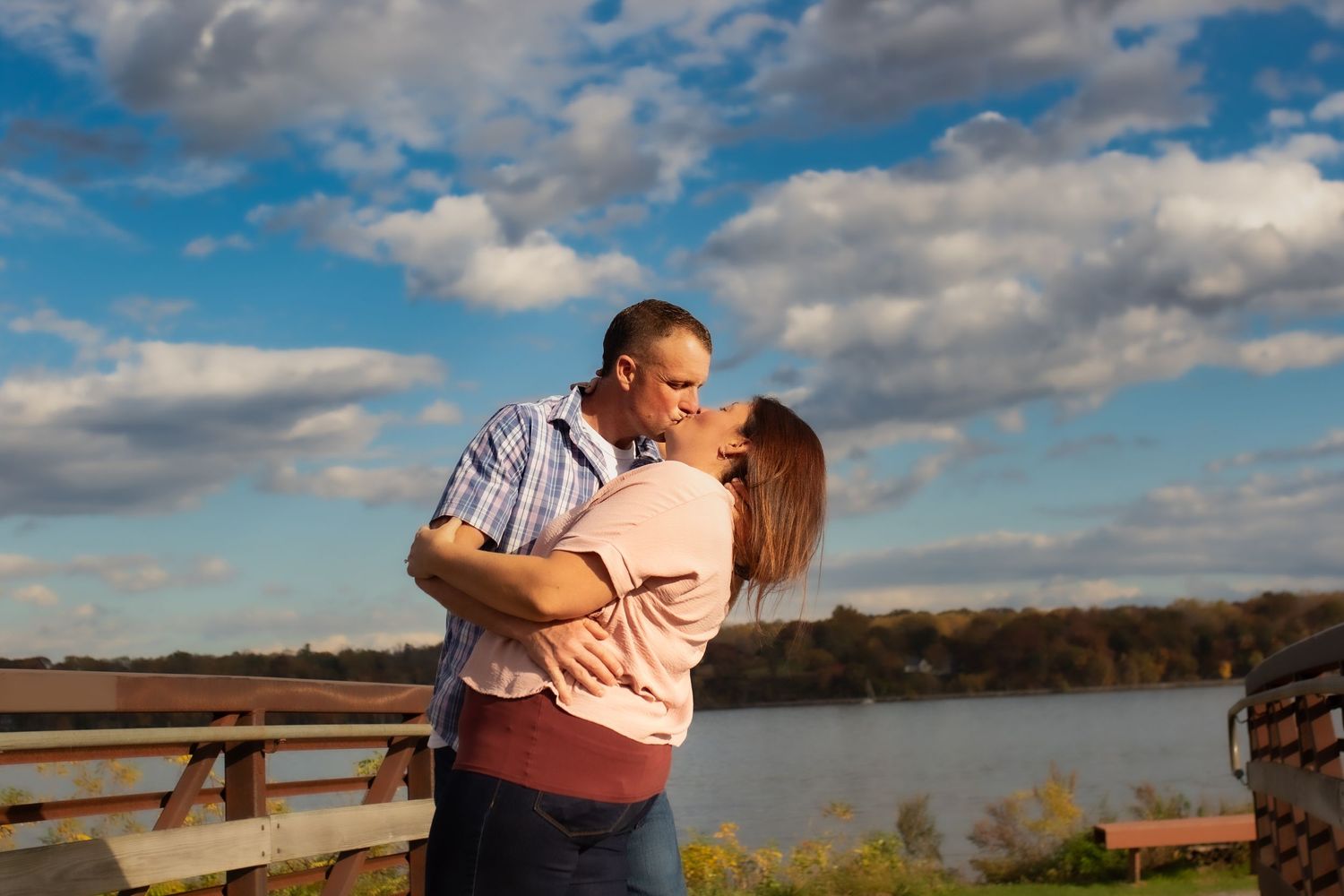 Couple embraces while laughing together on wooden deck by the lake.