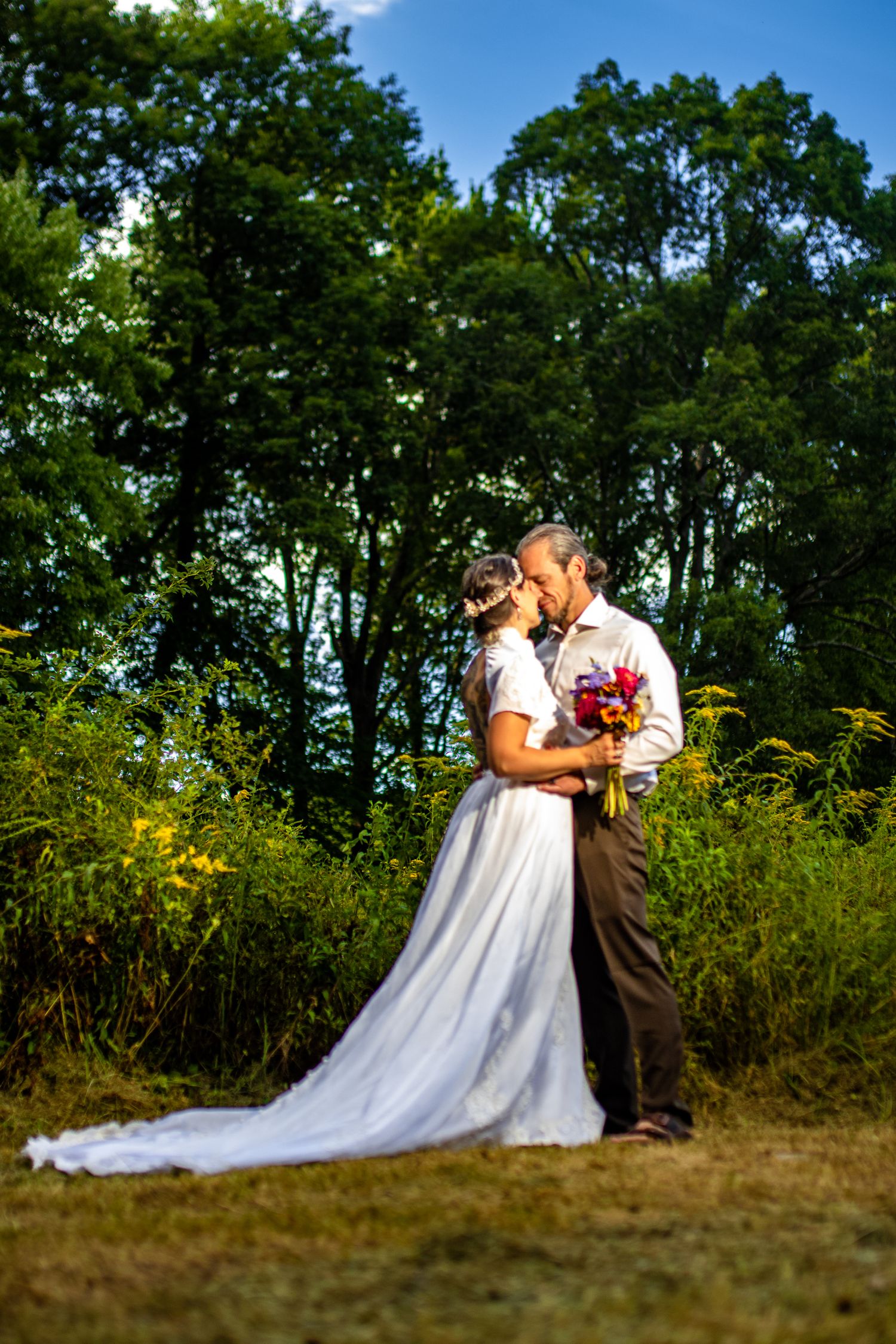 Romantic wedding portraits in field with wildflowers and trees.