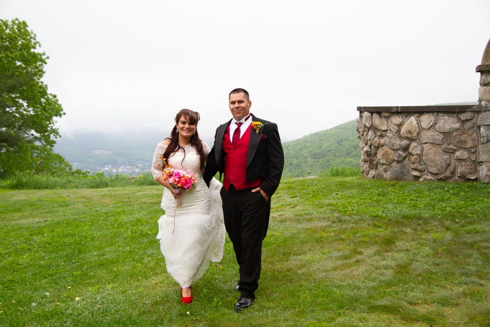 A couple walks together on a scenic grassy hillside overlooking mountains.