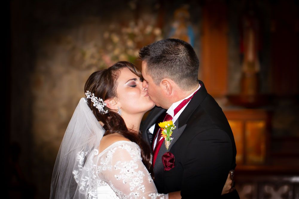A romantic wedding moment captured in warm lighting with red floral accents.