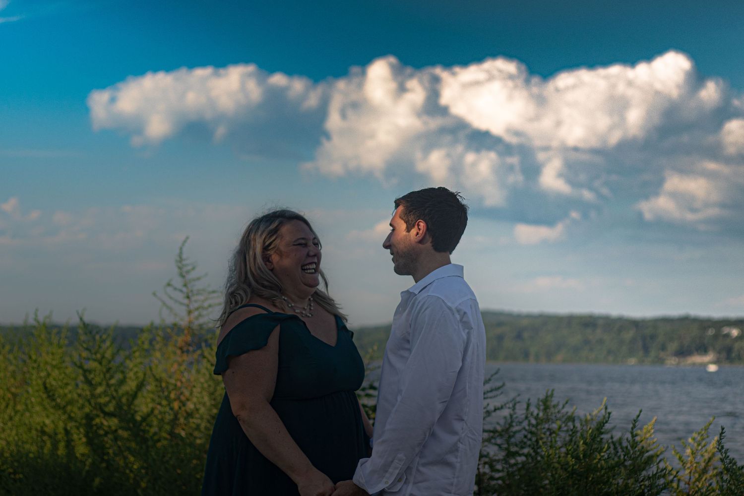 Scenic waterfront engagement photos with blue sky and clouds.