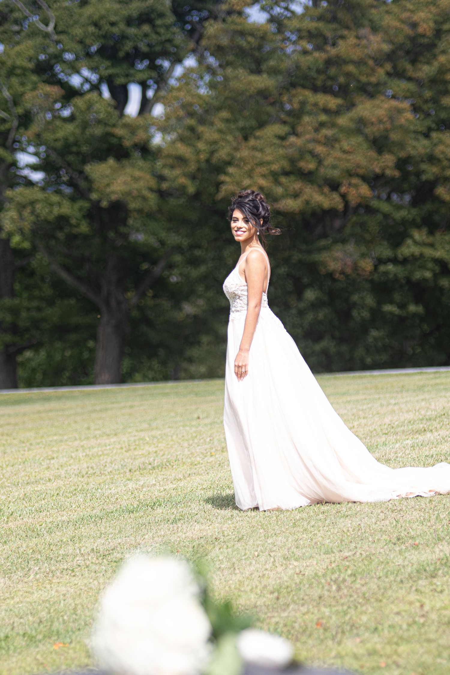 White wedding dress flowing in the breeze across a sunlit grassy hillside.