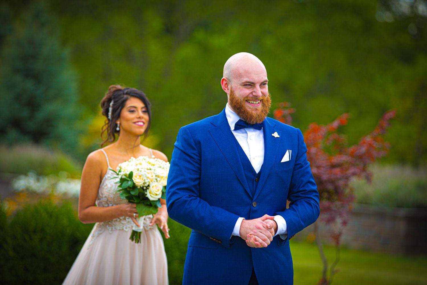 Wedding party poses in formal attire against lush garden background.