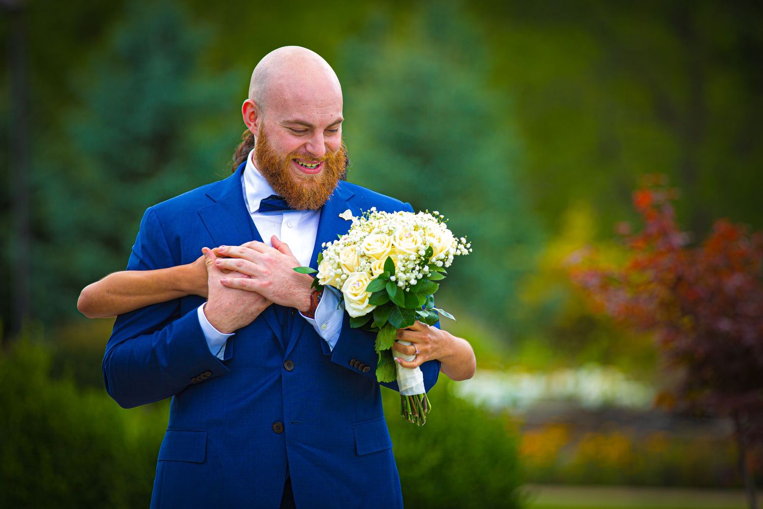 Wedding party members in blue suits and white bouquets against autumn foliage.