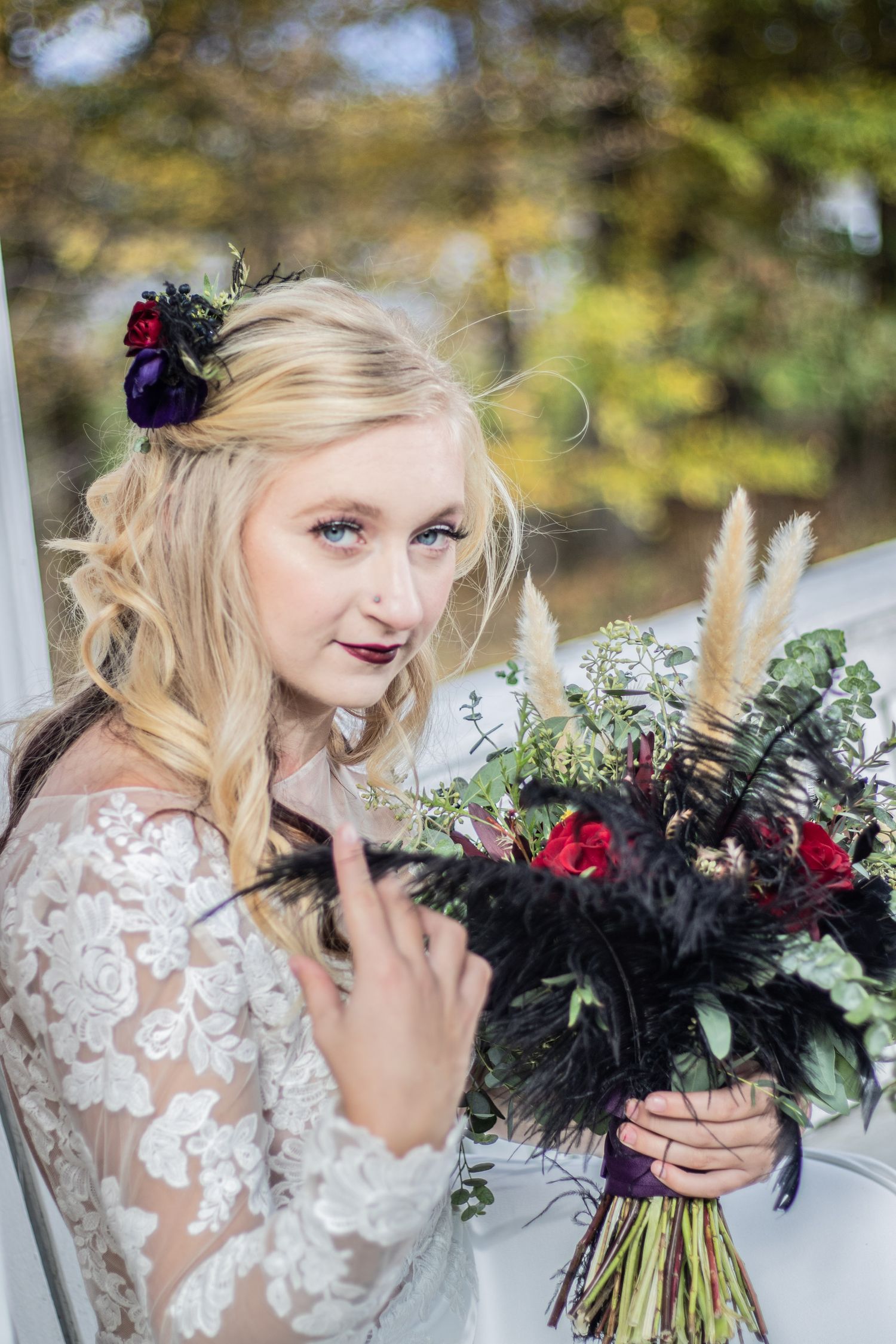 A bride holding a dramatic black and burgundy bouquet with feather accents.