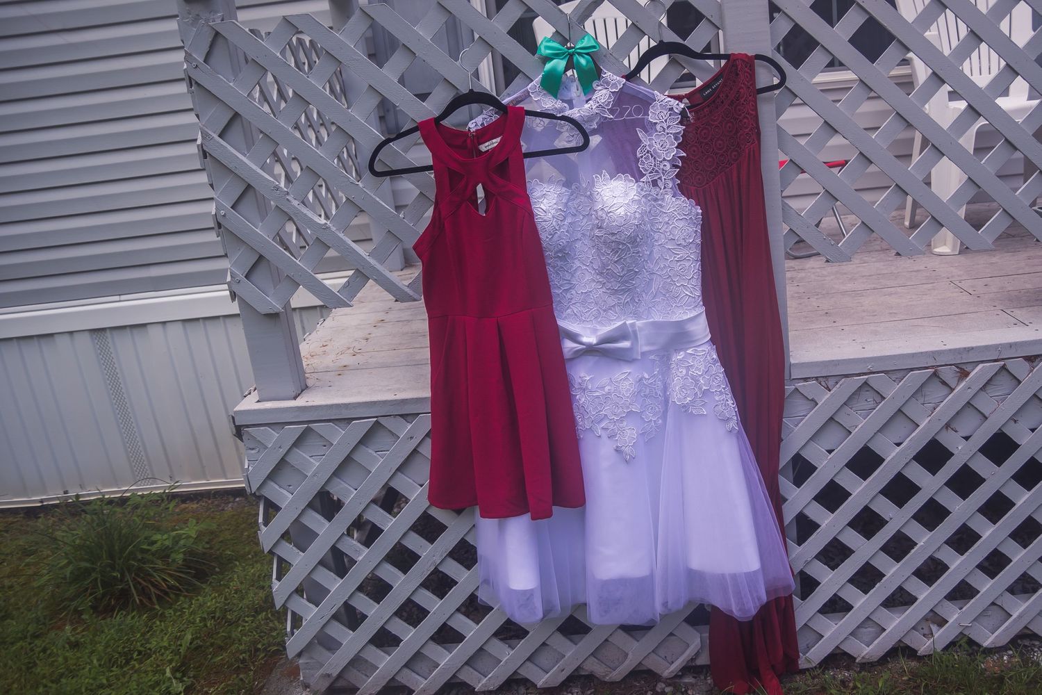White and red dresses hanging on lattice fence outdoors.