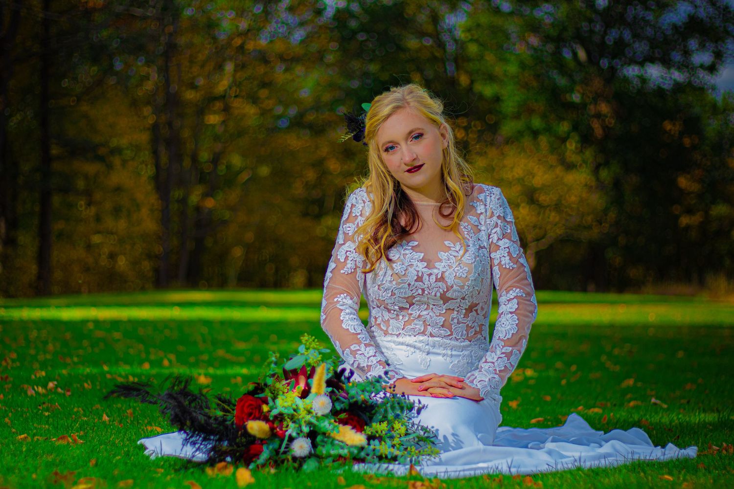 A bride in lace dress poses with gothic-inspired floral bouquet on autumn grass.