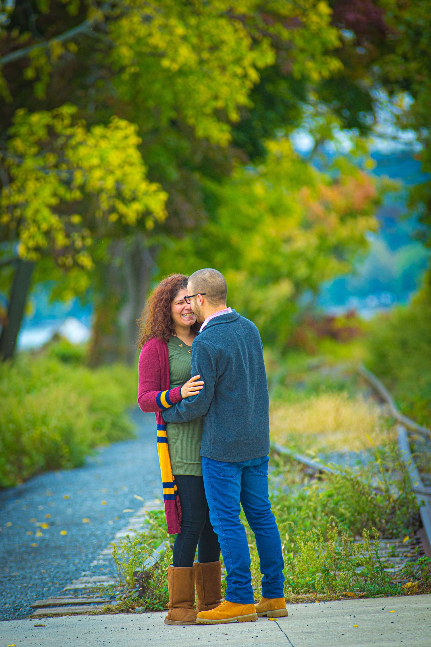 Couple walking along scenic path with vibrant green trees and blue water in background.