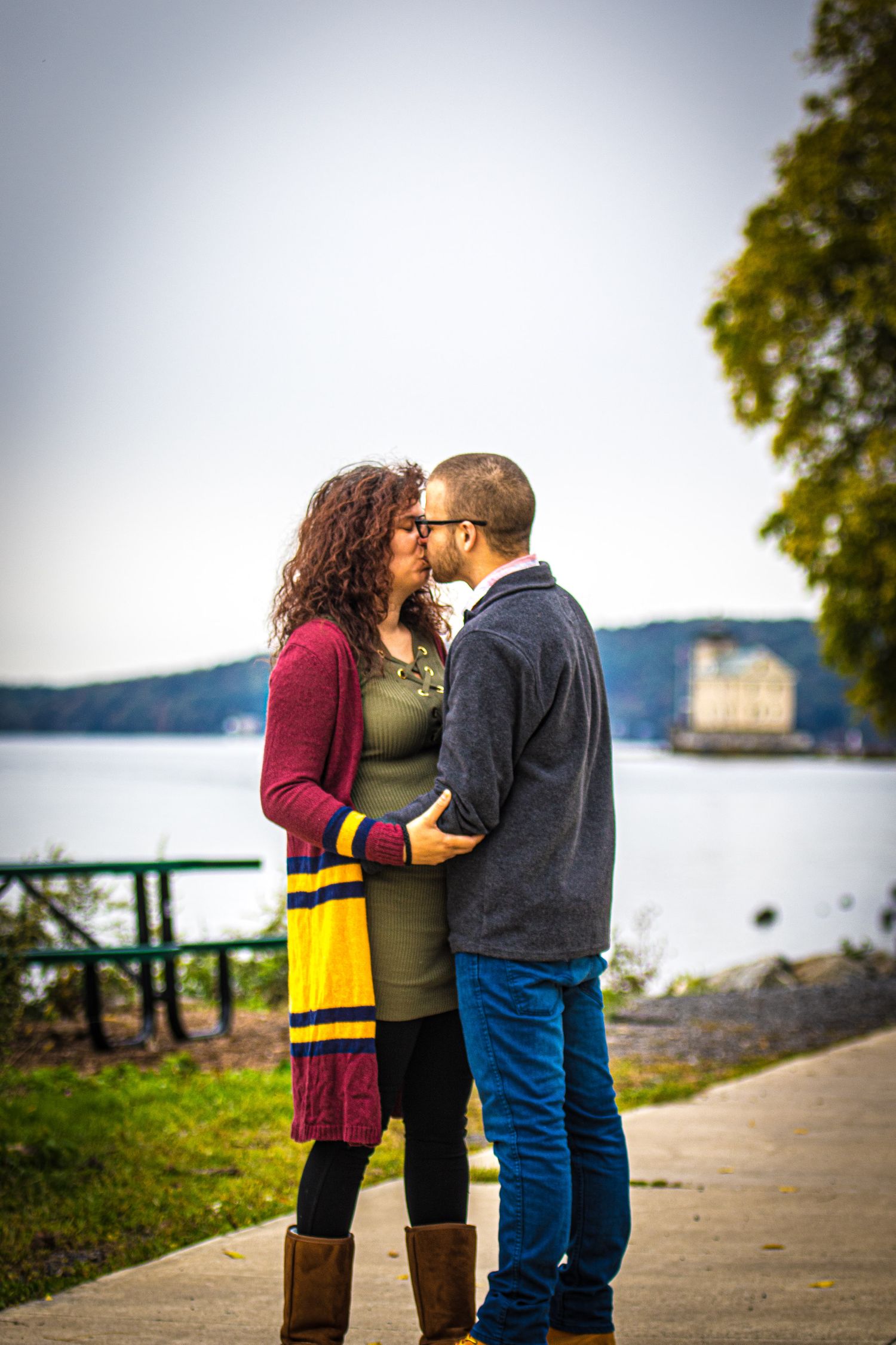 Romantic moment captured on waterfront path with mountains and trees in background.