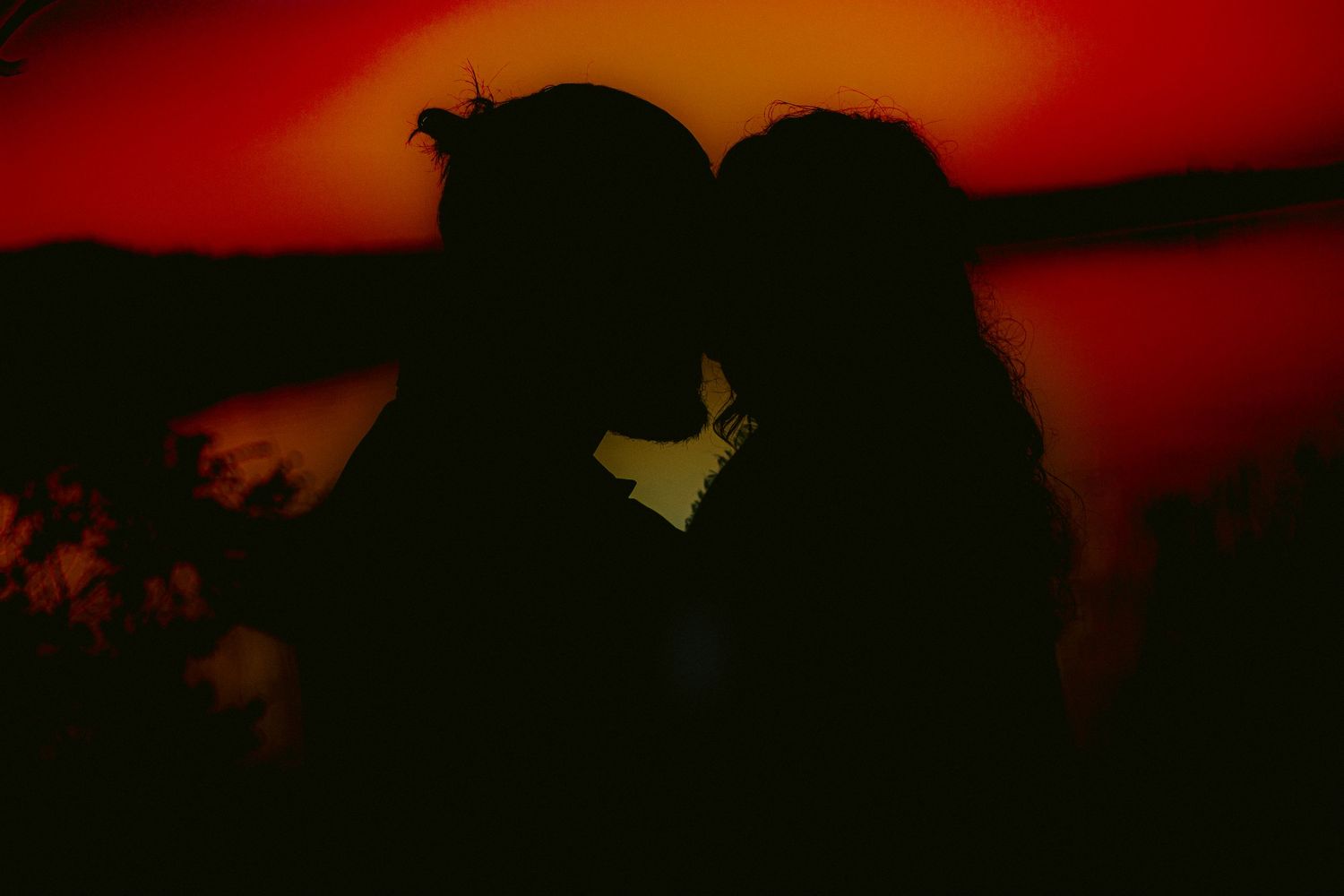 Silhouettes against dramatic red sunset sky during outdoor photo session.
