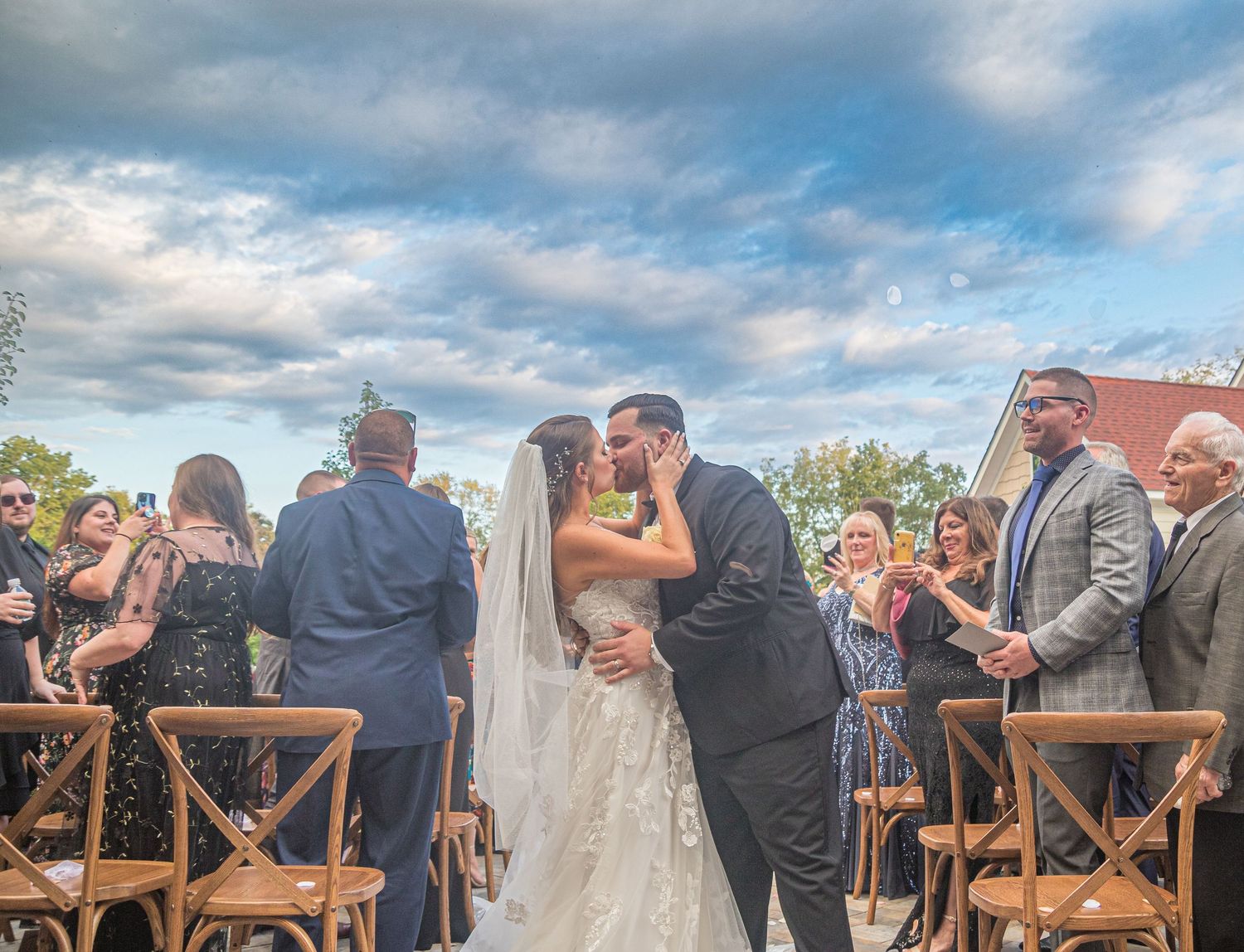 Wedding ceremony guests seated in wooden chairs during an outdoor celebration.