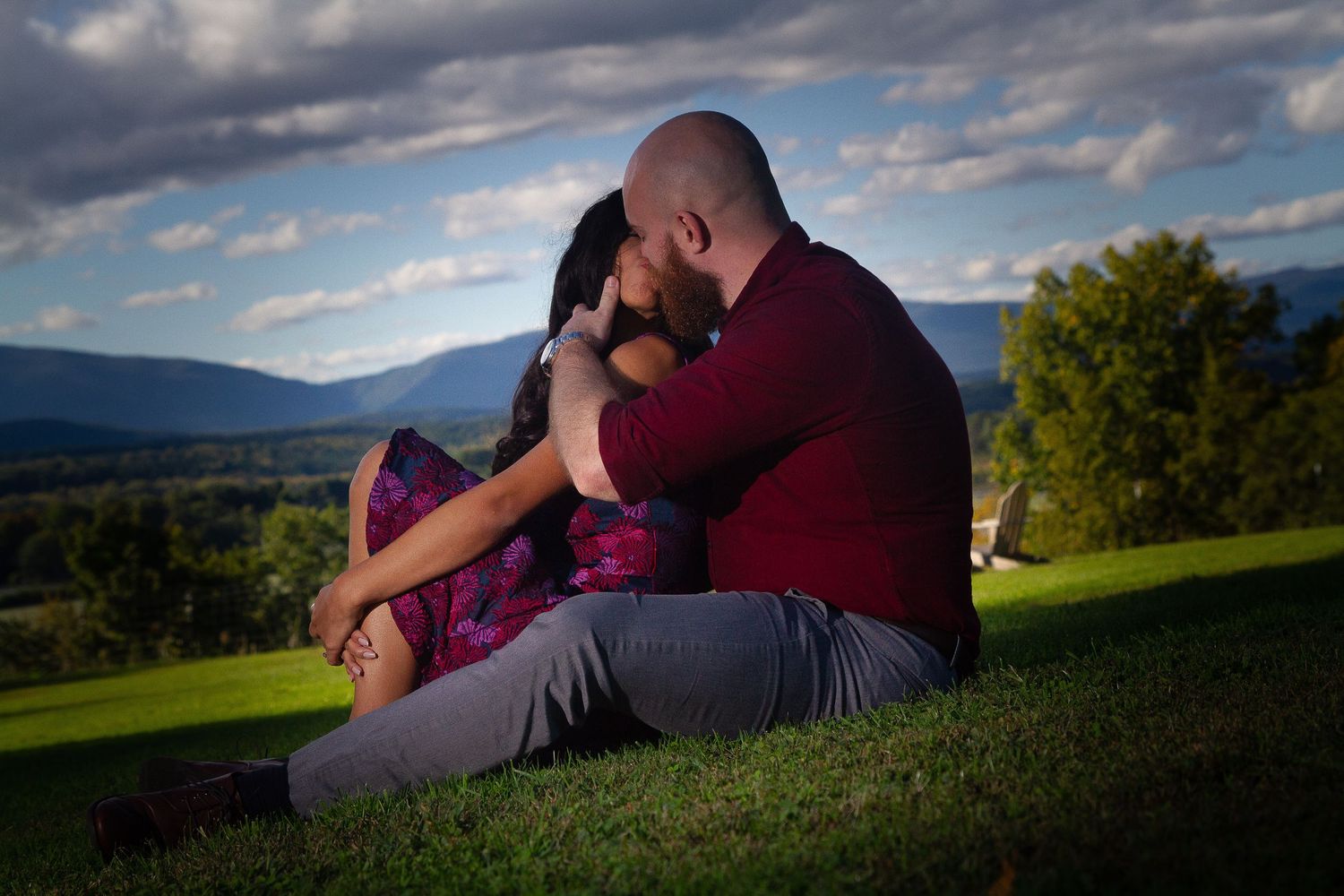 Couple relaxing on grassy hill during sunset with dramatic cloudy sky in background.