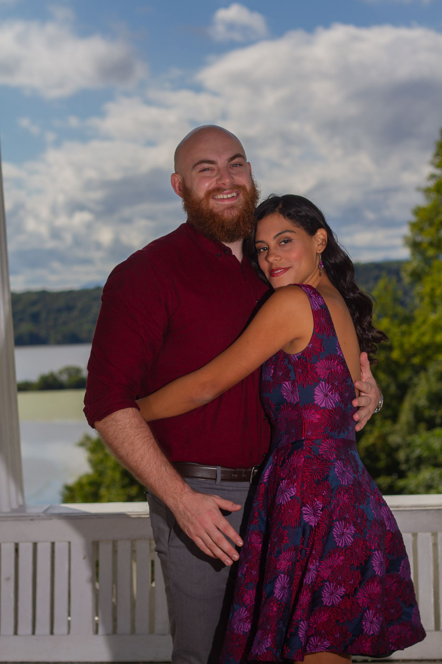 A couple embraces on a deck overlooking a scenic lake on a cloudy day.