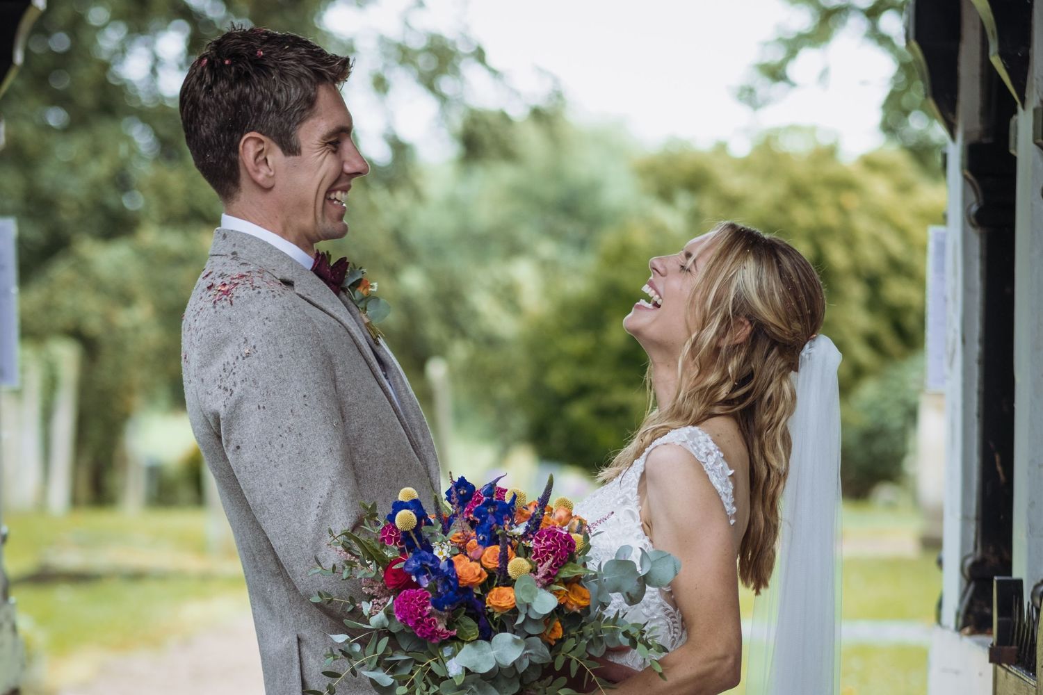A couple shares a joyful moment while holding a vibrant bouquet of flowers outdoors.