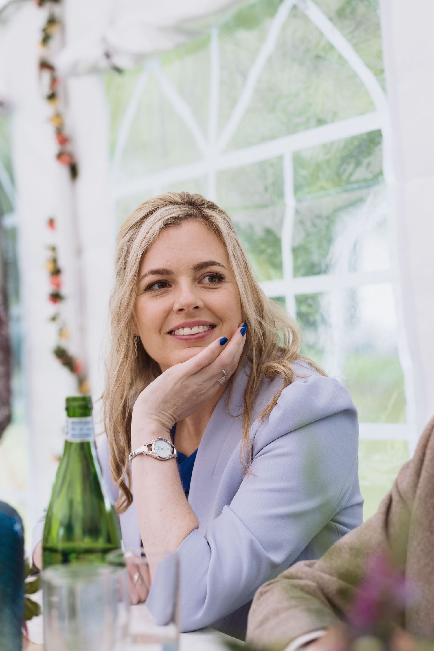 A guest in a lavender blazer smiles while seated at a decorated table.