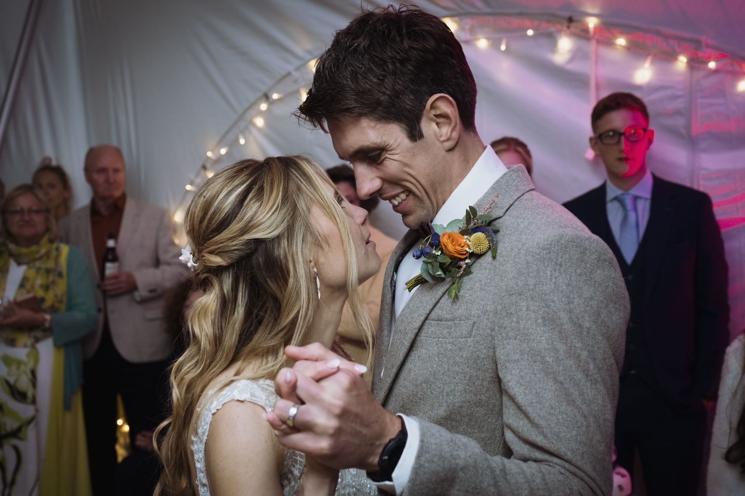 A couple shares their first dance under twinkling lights at their wedding reception.