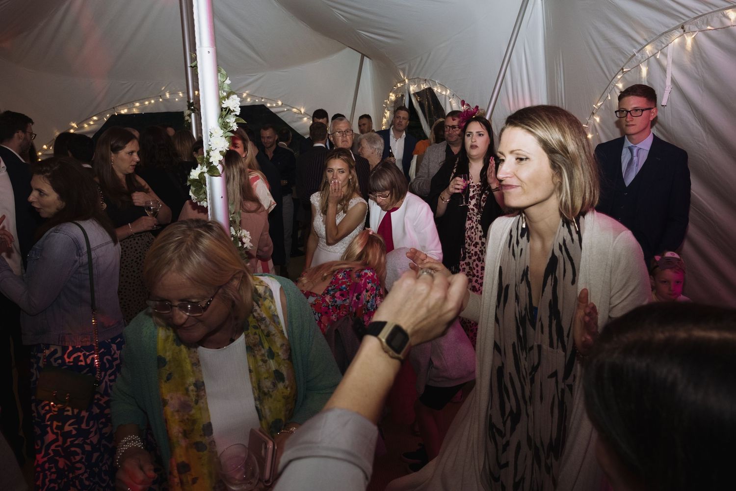 Guests dancing and celebrating at a lively wedding reception under a tent.