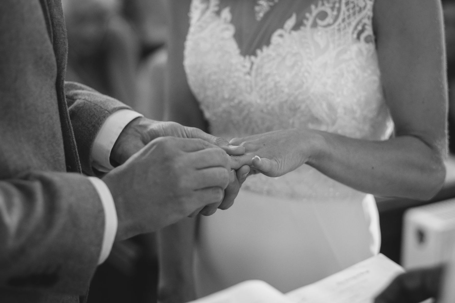 Black and white close-up of hands exchanging wedding rings during a ceremony.