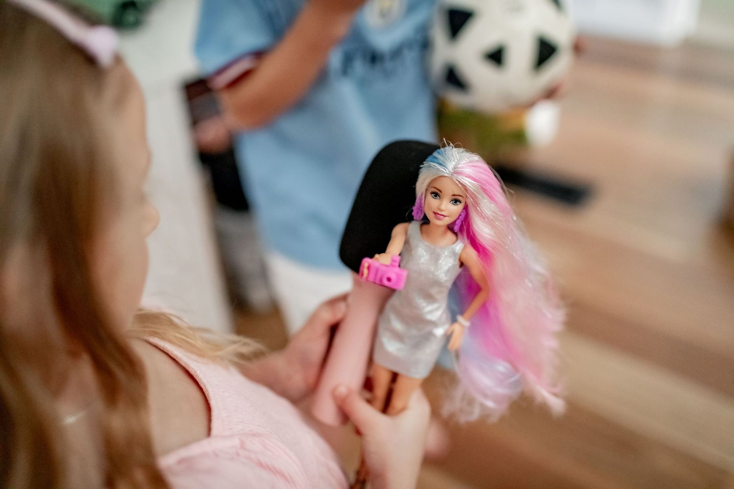 Close-up view of Barbie doll with pink hair being held up against wooden floor background.