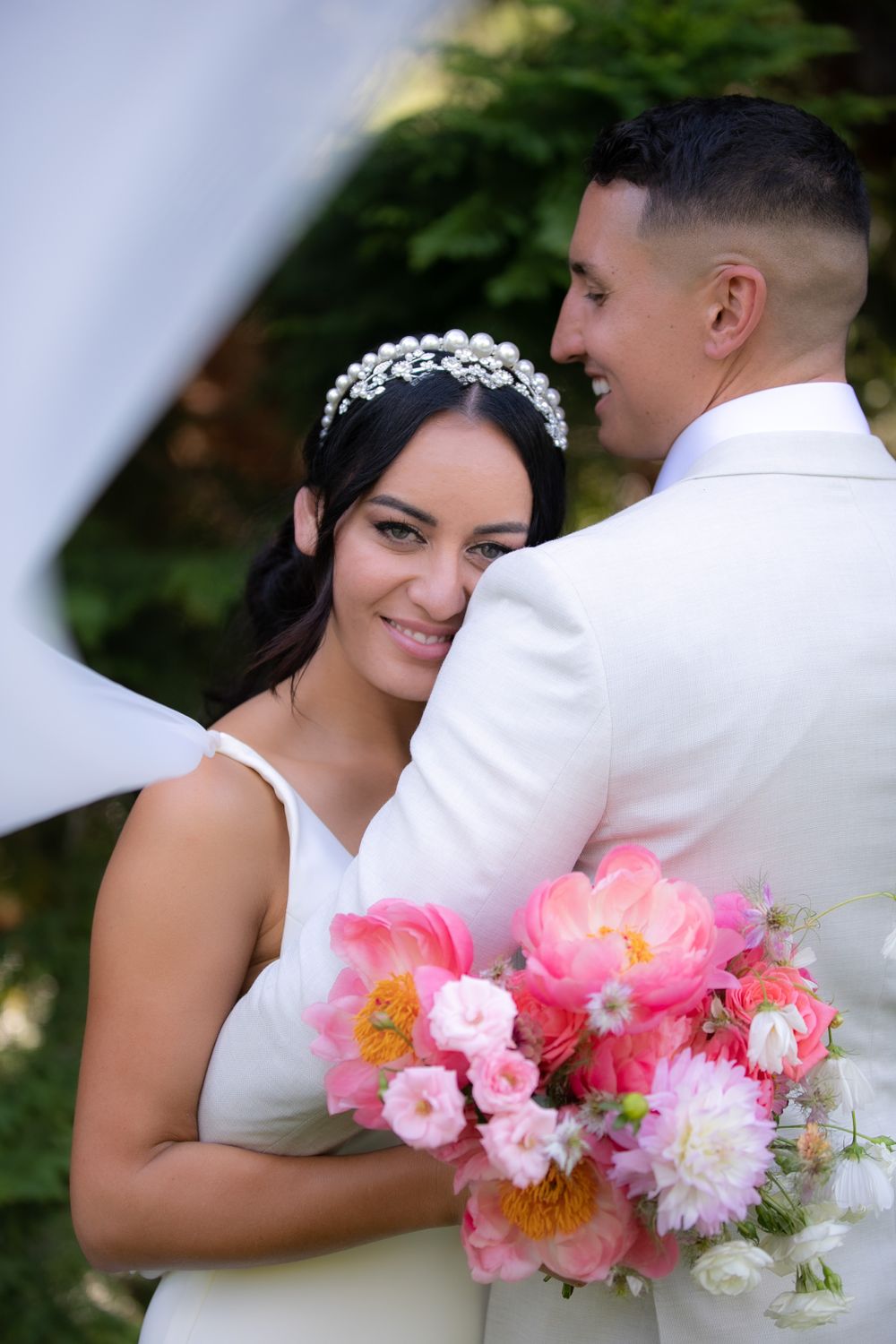 Romantic wedding portrait with pink and white bouquet under white veil outdoors.