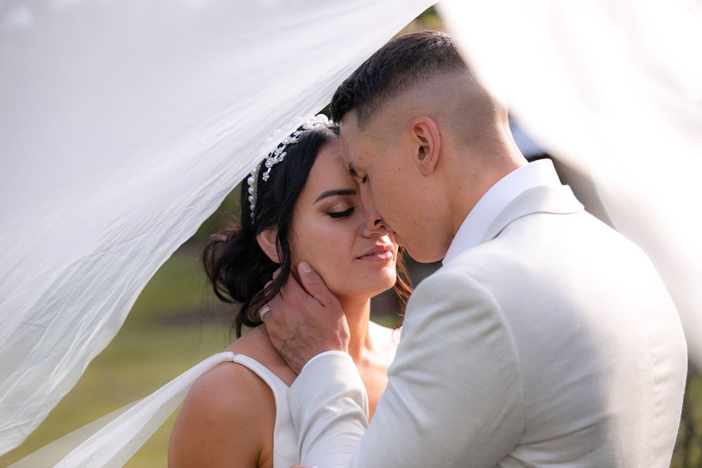 Intimate wedding portrait under flowing white veil with soft lighting.