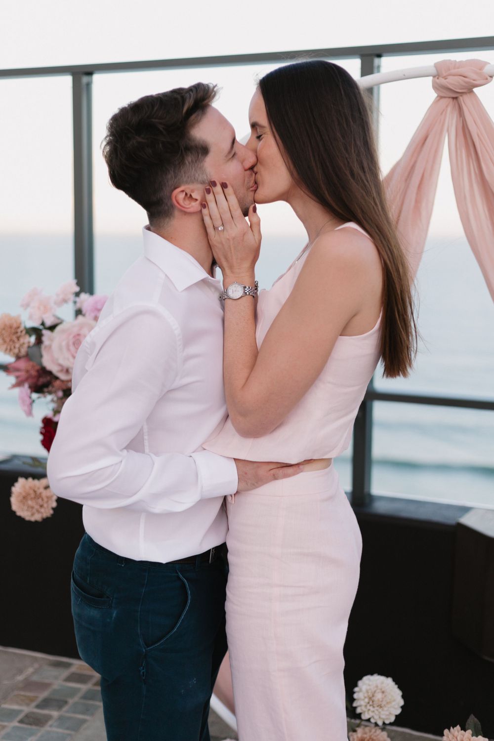 A romantic embrace captured on an oceanfront terrace decorated with pink fabric and flowers.