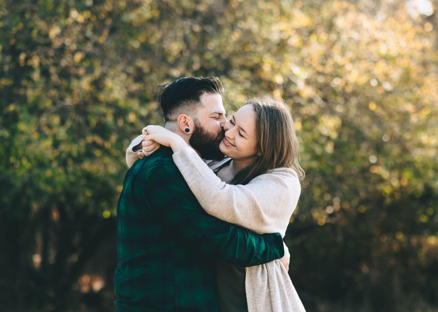 A tender moment between two people wearing green and white in an autumn setting.