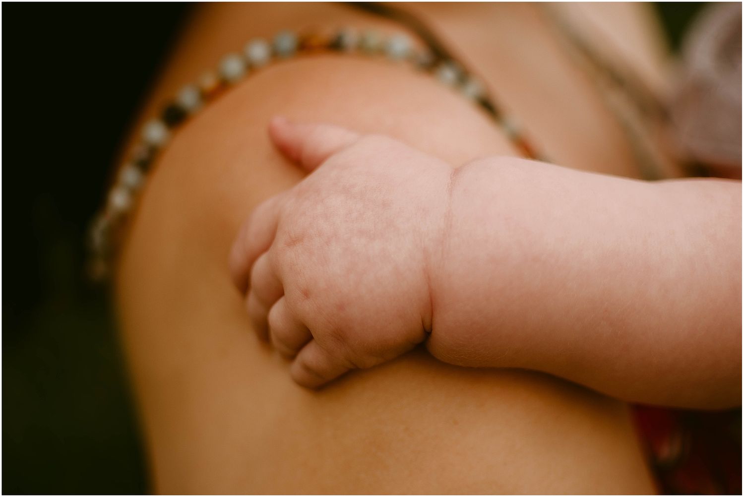 Close-up photo of small baby hand resting on arm with bracelet.