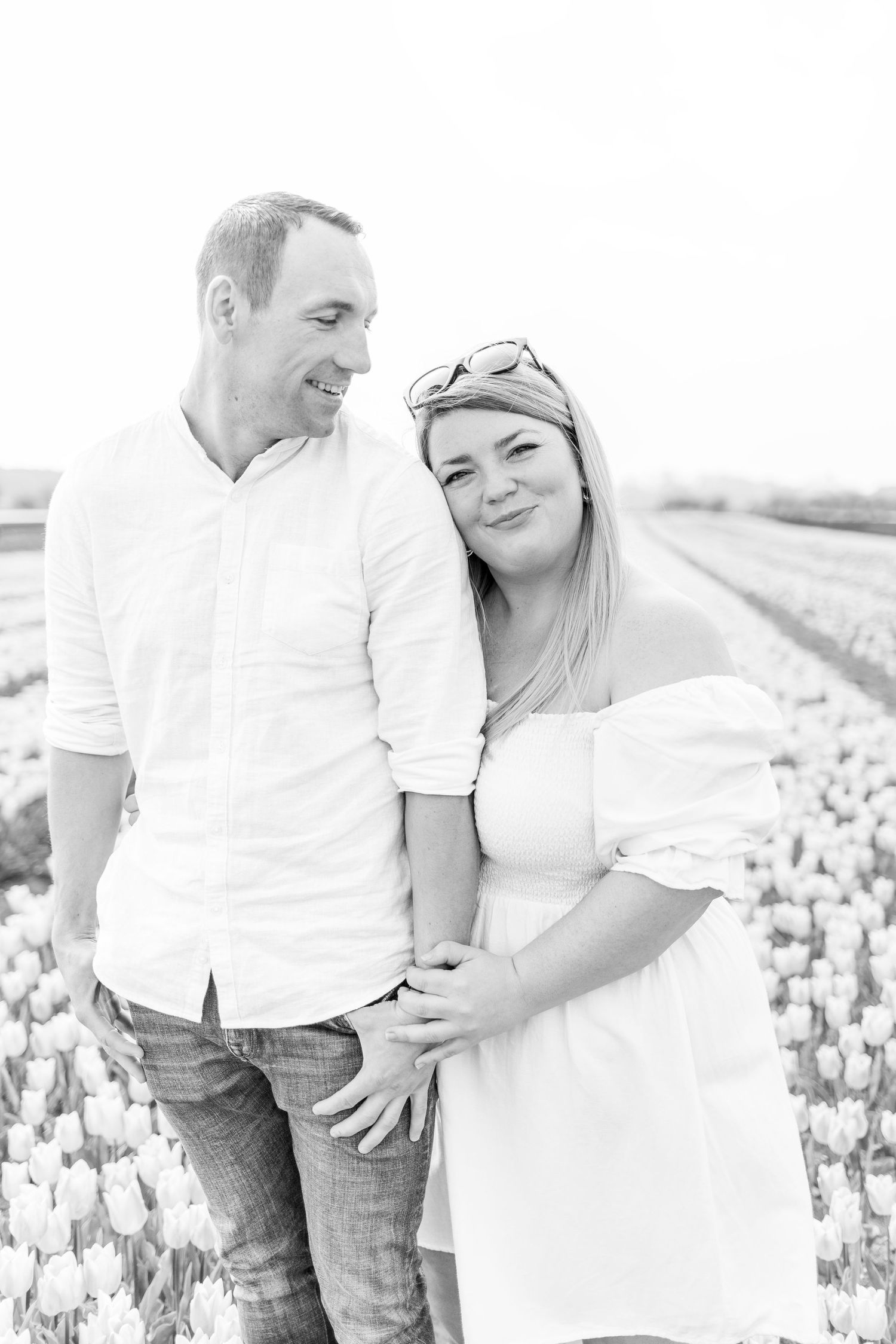 Couple in casual white outfits sharing an intimate moment among blooming tulip fields.