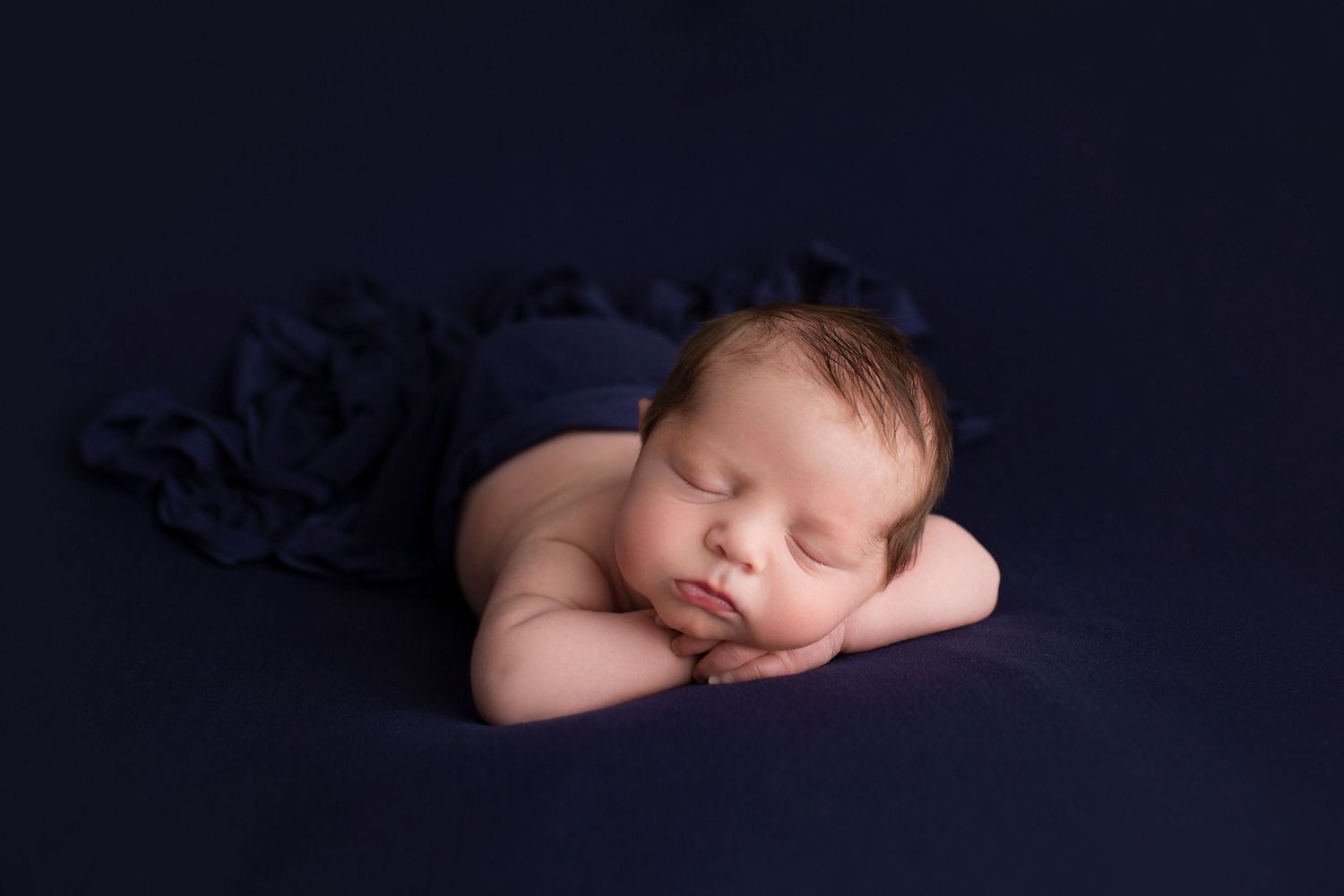 Peaceful newborn sleeping on dark blue fabric in studio setting.