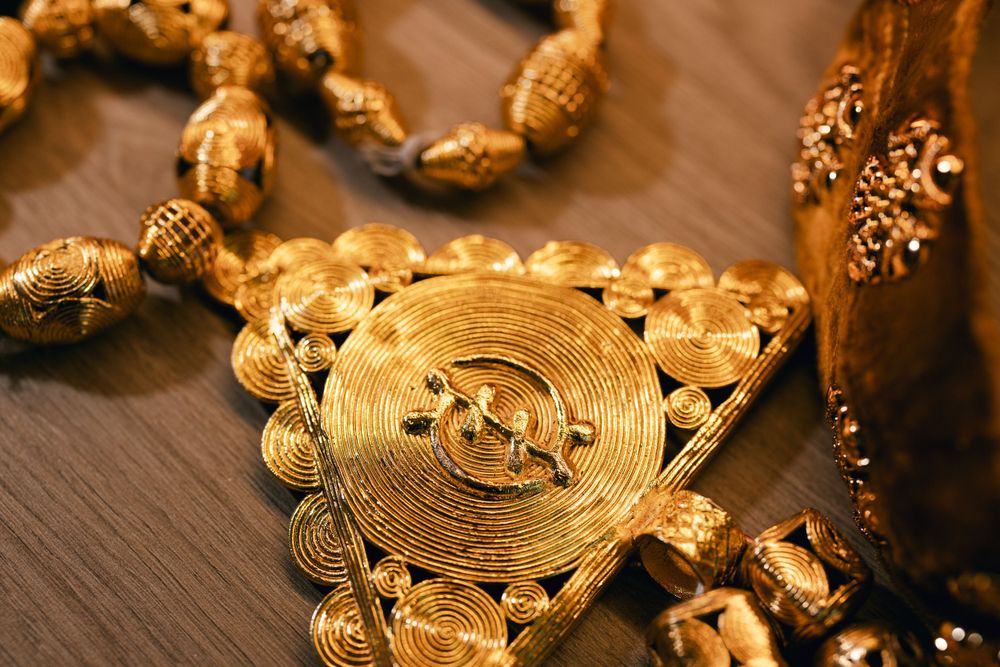 Ornate golden circular pendant necklace with intricate traditional design on wooden surface.