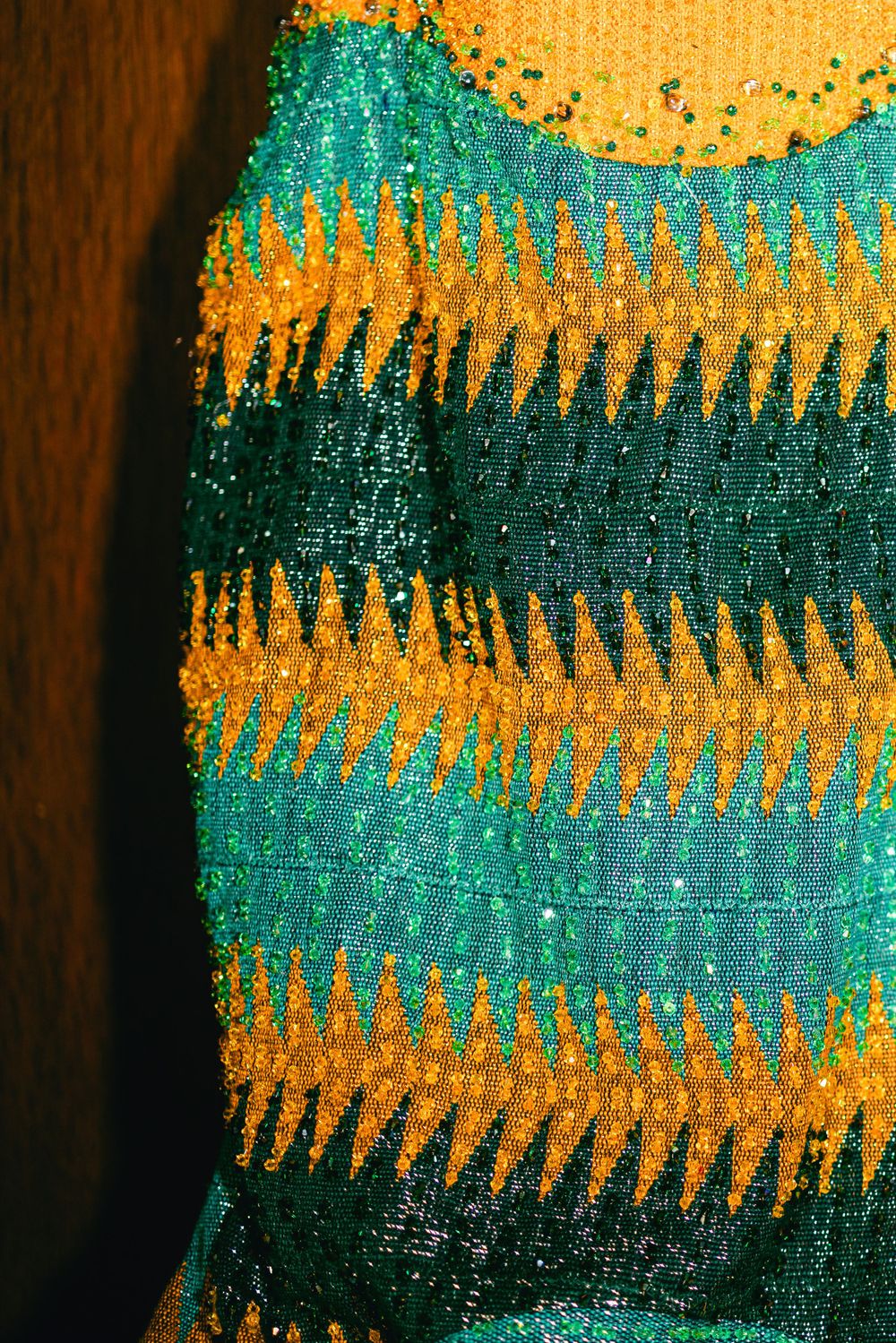 Close-up of a striped fabric pattern in turquoise and golden yellow with intricate beaded details.