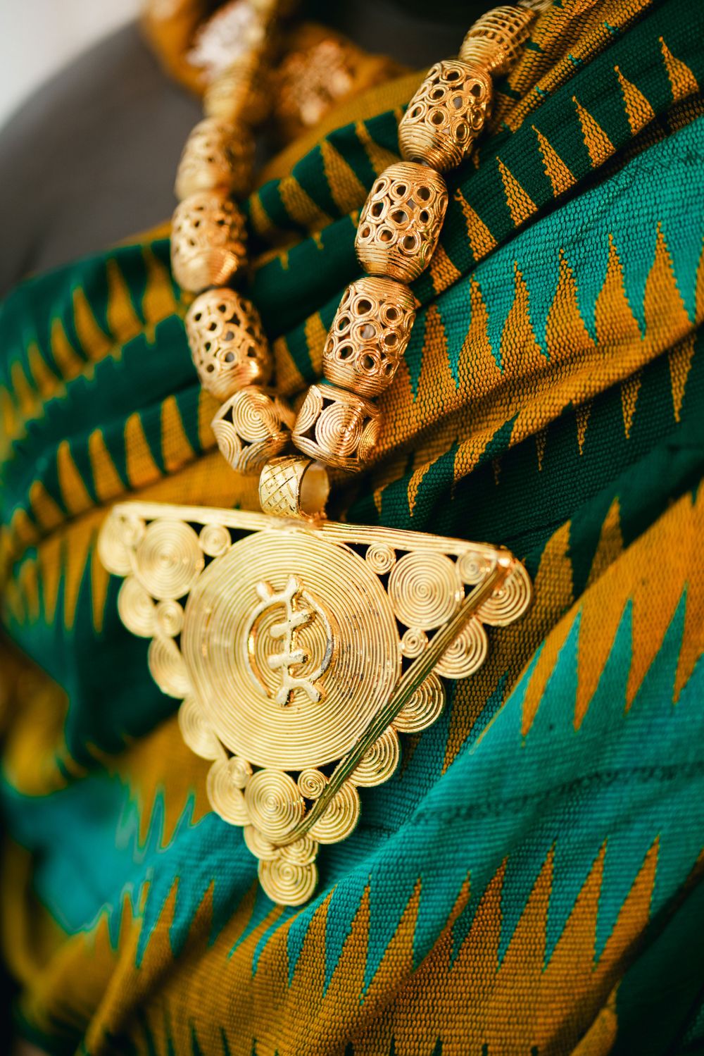 Close-up of ornate gold jewelry and traditional green kente cloth with geometric patterns.