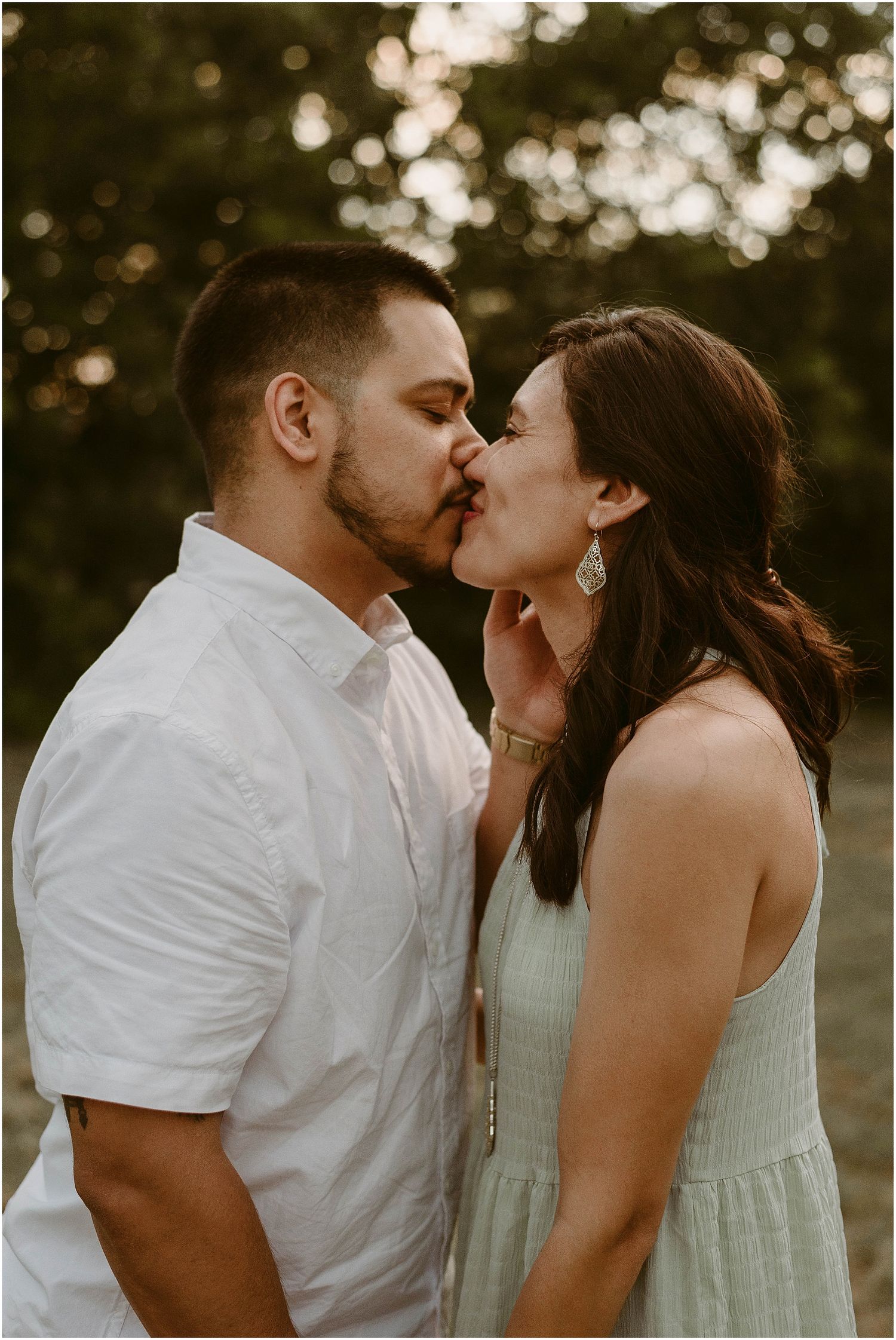 A romantic couple sharing a tender kiss at sunset in an outdoor setting.
