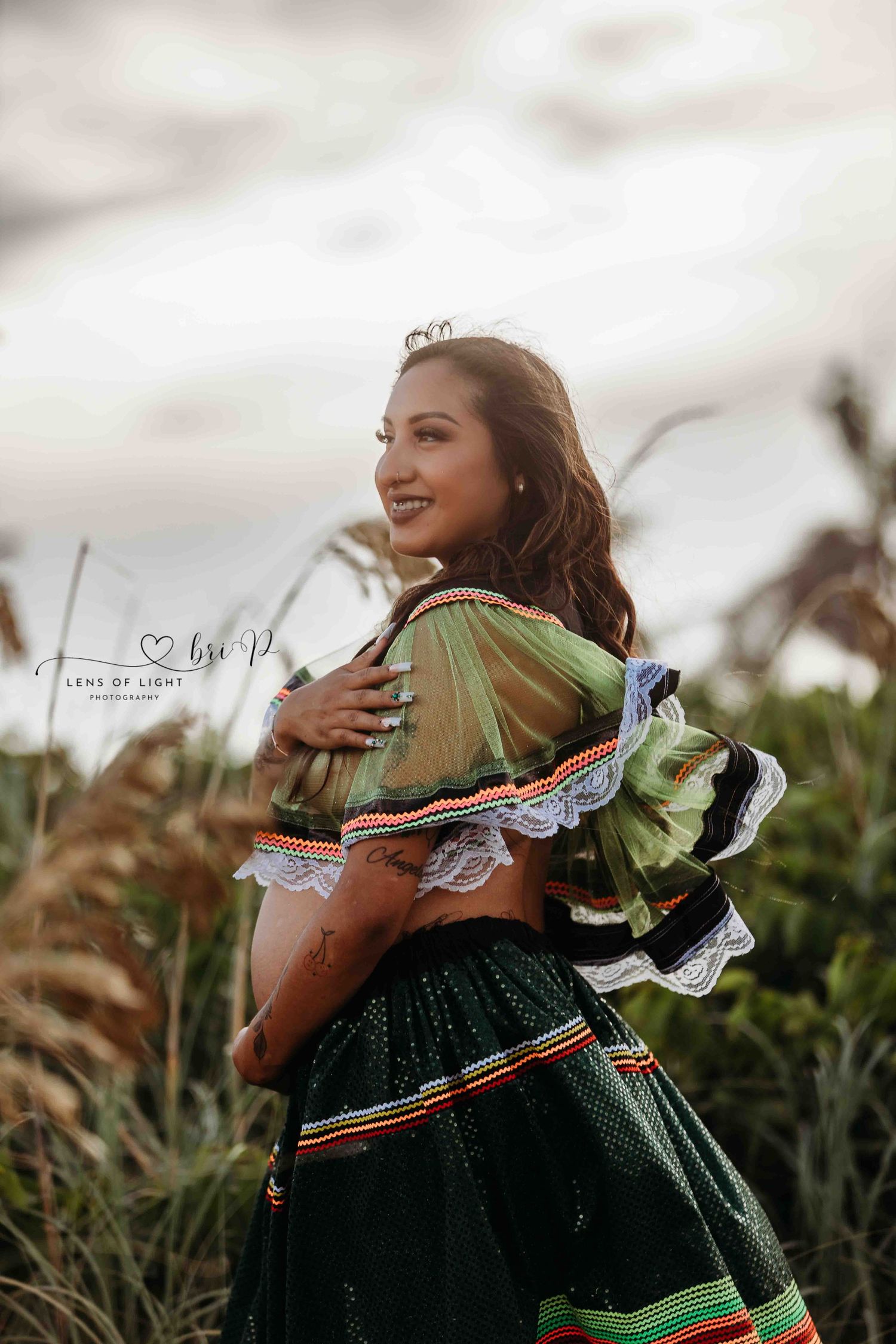 Traditional green dress with colorful trim photographed in a field during golden hour with a dreamy atmosphere.