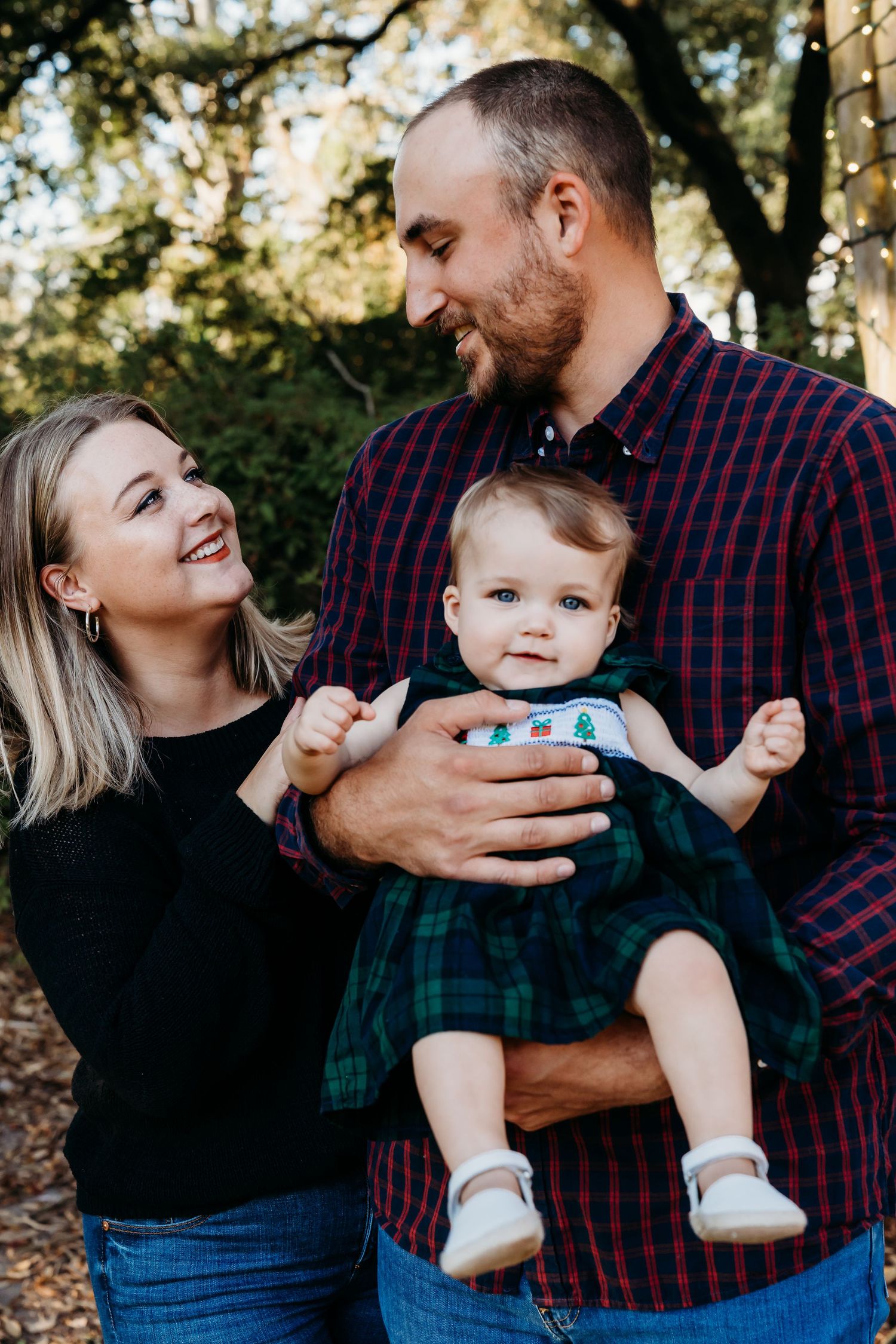 Happy family moment outdoors with baby wearing plaid dress.