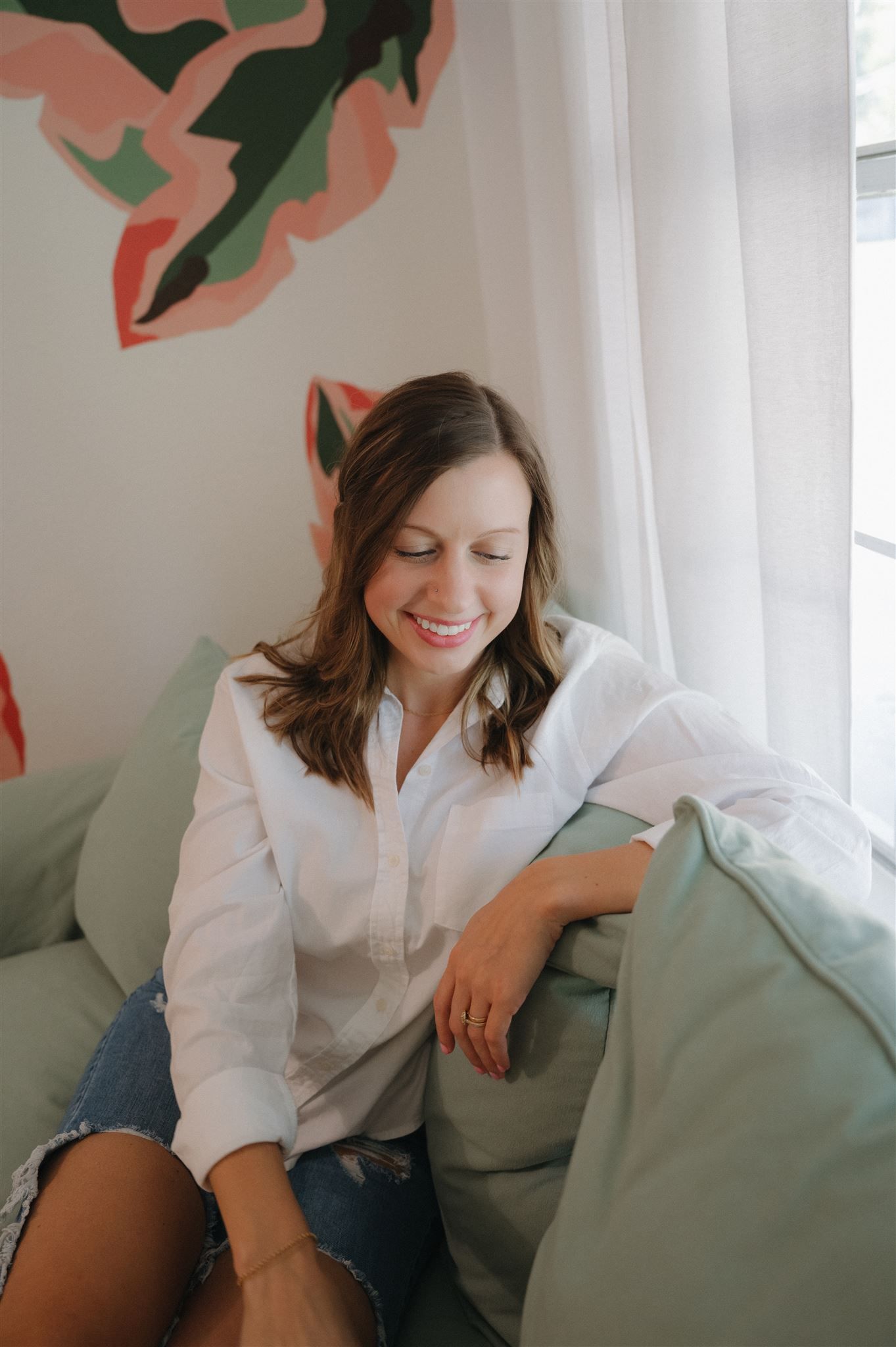 Woman in white button-down shirt relaxing on gray couch with decorative wall art in background.