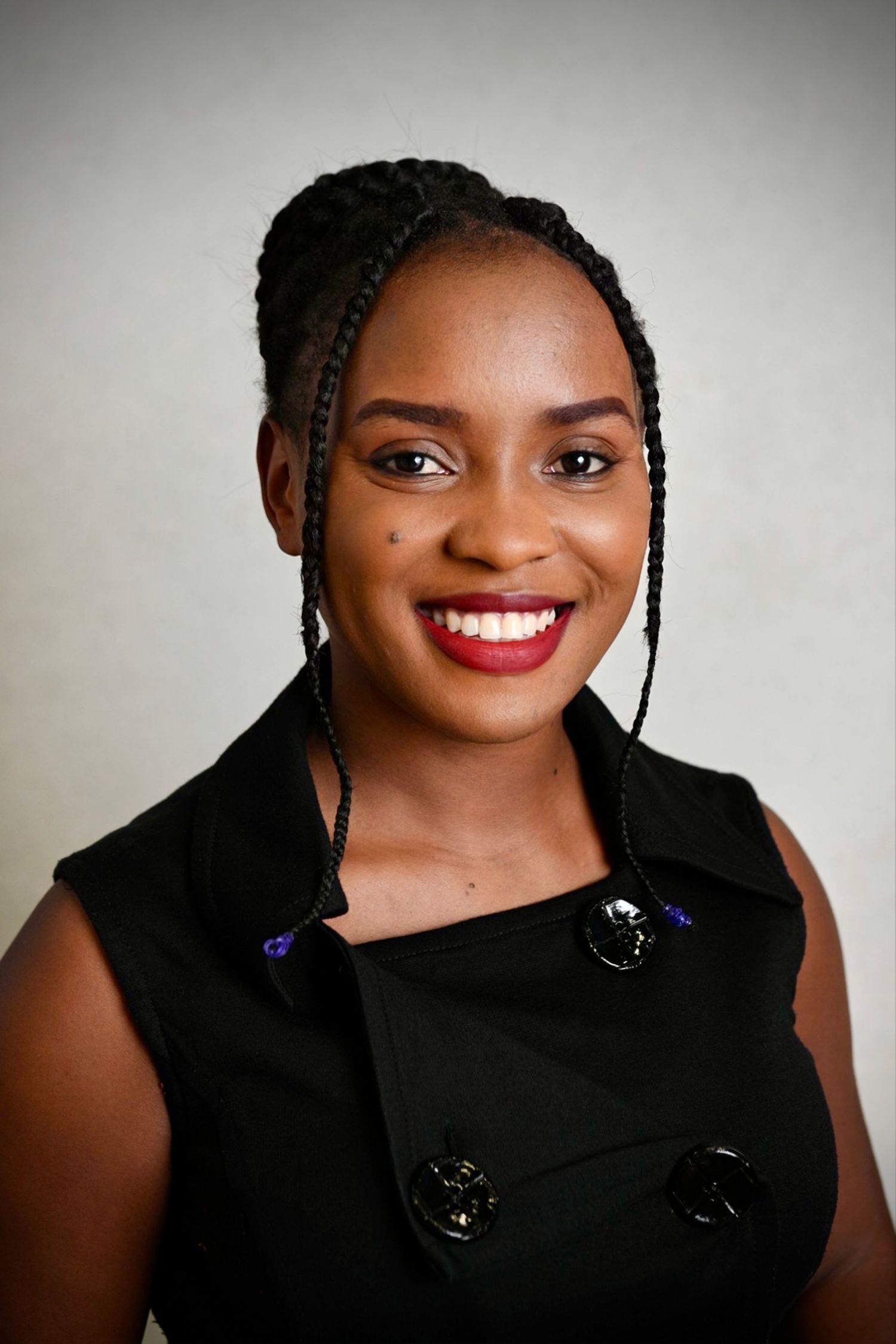 Professional portrait of person wearing black sleeveless top with braided hair and bright smile.