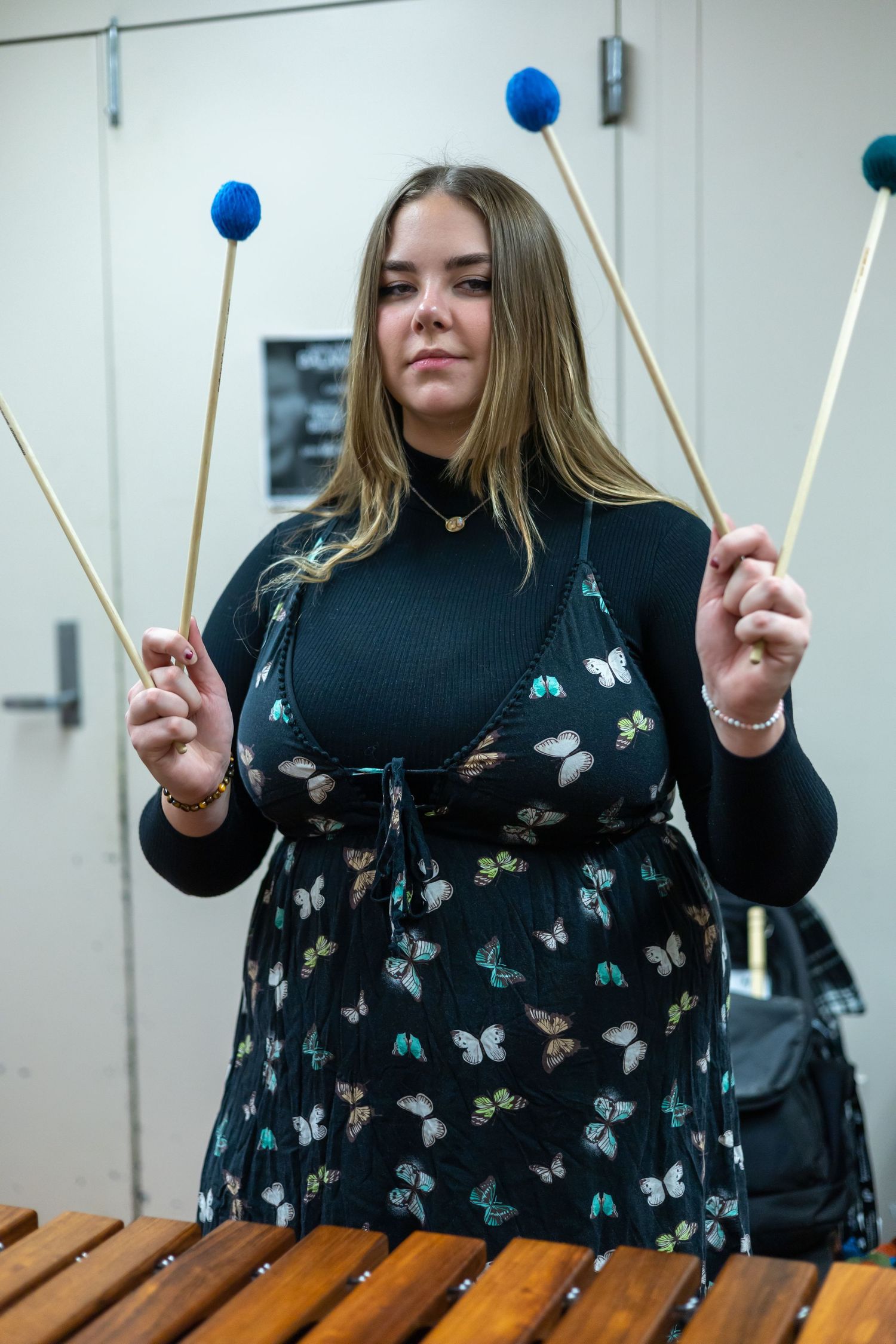 Musician playing xylophone with mallets wearing butterfly-patterned top against white background.