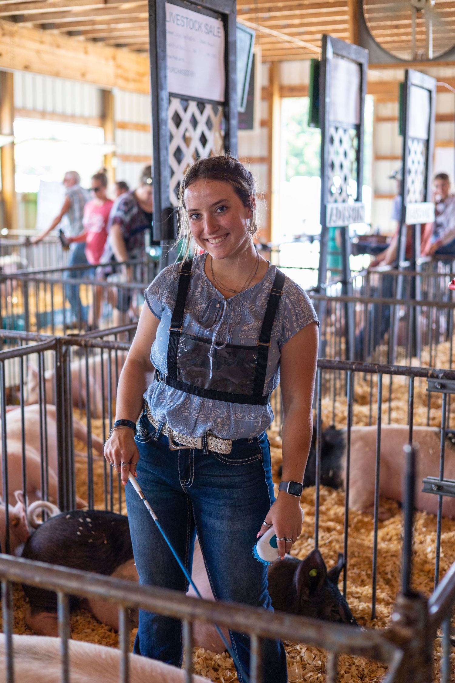 People in denim overalls tending to animals in a barn setting with natural lighting.