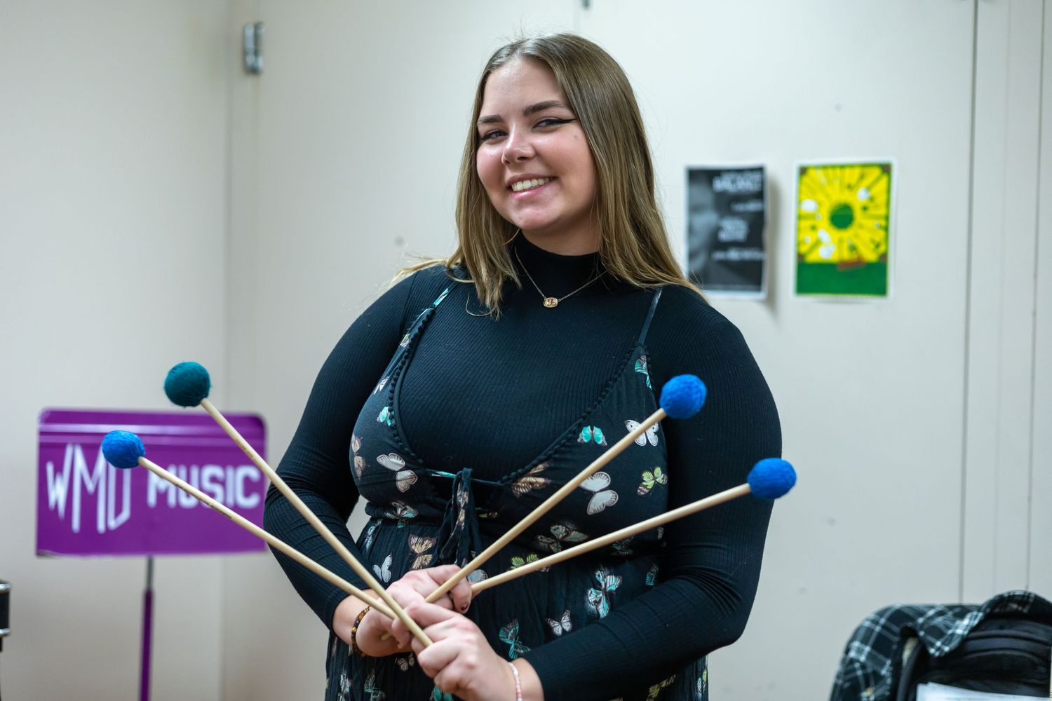 Percussionist performing on marimba in music classroom with colorful posters on wall.