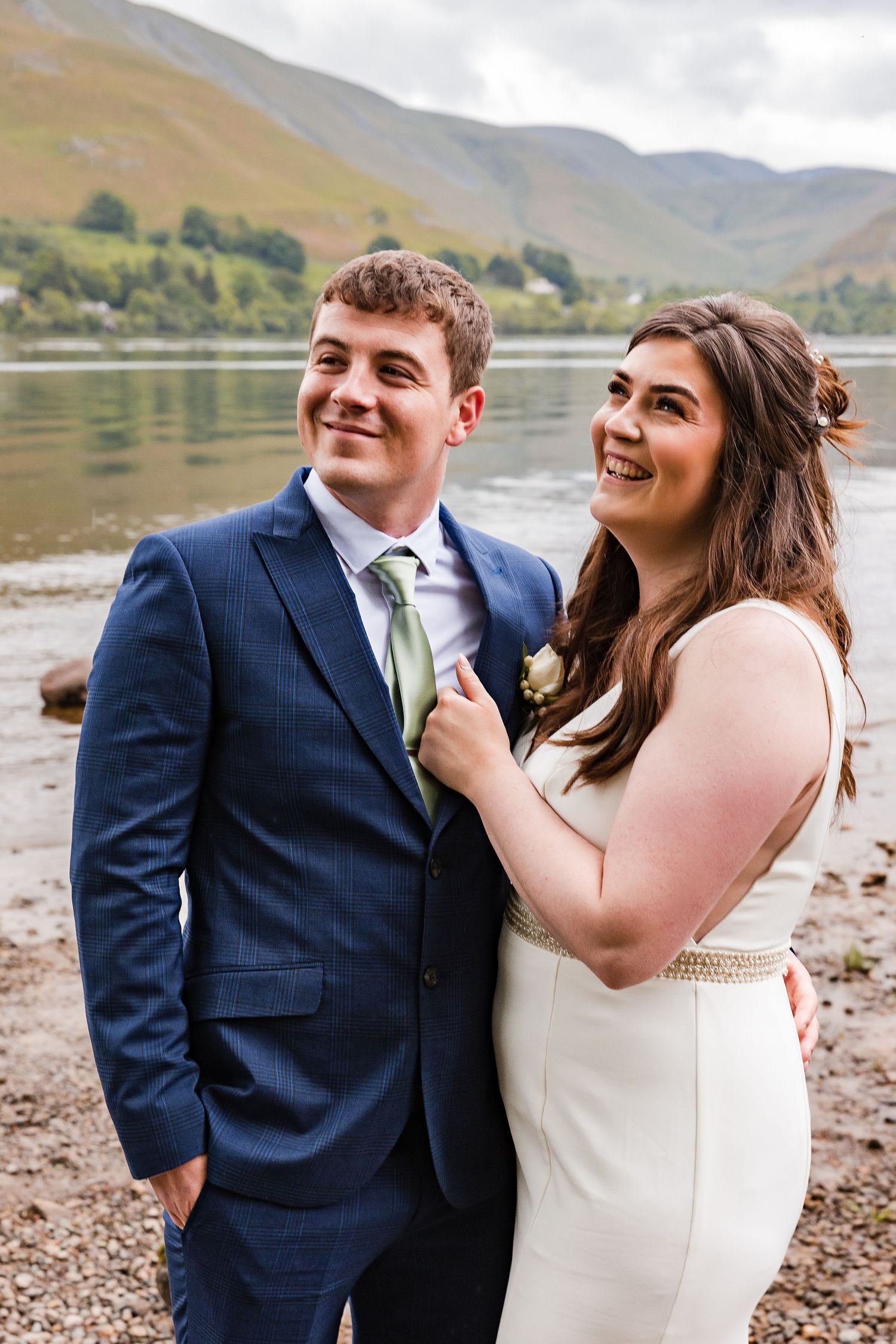 Newlywed couple posing by a serene lake with mountains in the background.