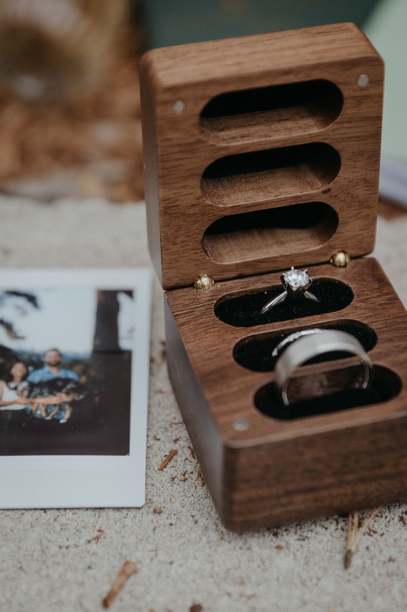 Wooden ring box with engagement ring and wedding bands displayed alongside a polaroid photo.