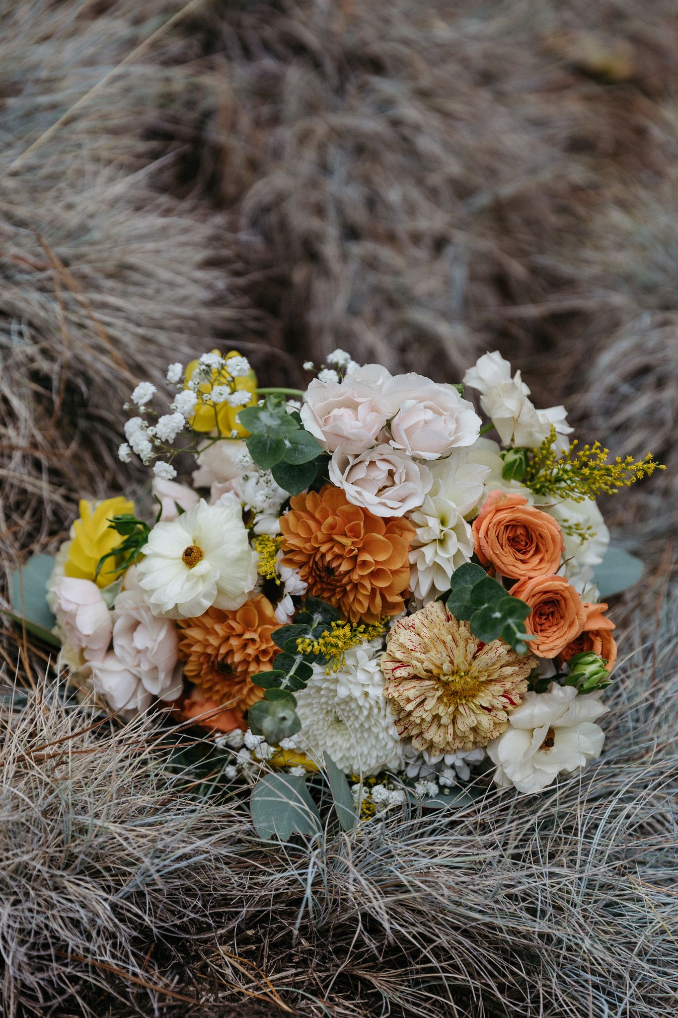 Rustic wedding bouquet featuring orange, white and yellow flowers with greenery accents.
