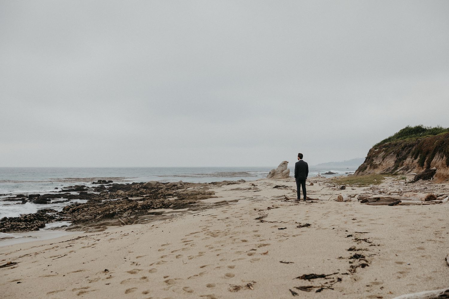 Lone figure walks along a misty rocky beach coastline.