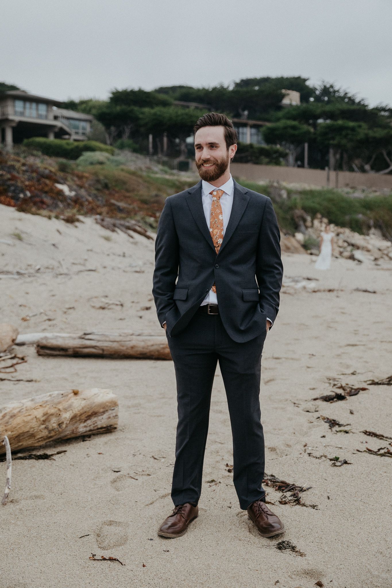 Formal attire on a cloudy beach with coastal homes in background.