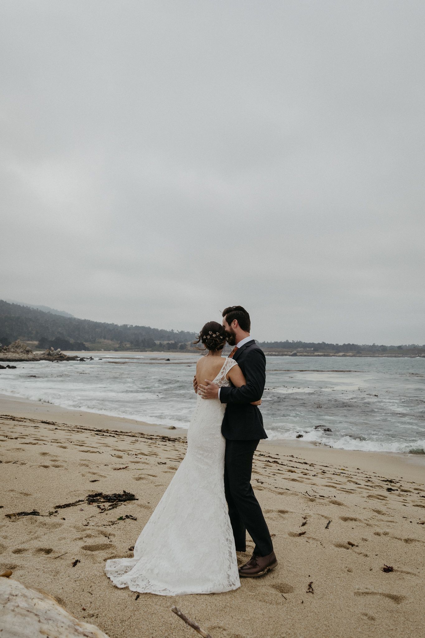 Intimate beach wedding moment captured against cloudy coastal backdrop.